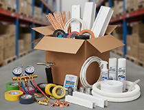 Cutie de carton deschisă pe podeaua depozitului înconjurată de accesorii meniu și diverse unelte HVAC, inclusiv benzi, calibre, țevi, tuburi și spray-uri. Rafturi cu cutii de accesorii în fundal.