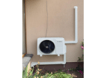 Un aparat de aer condiționat Bosch pentru exterior este montat pe un perete bej cu țevi albe și un Canal mascare traseu aer conditionat CLM 60x45 care ascunde țevile, cu plante în apropiere.